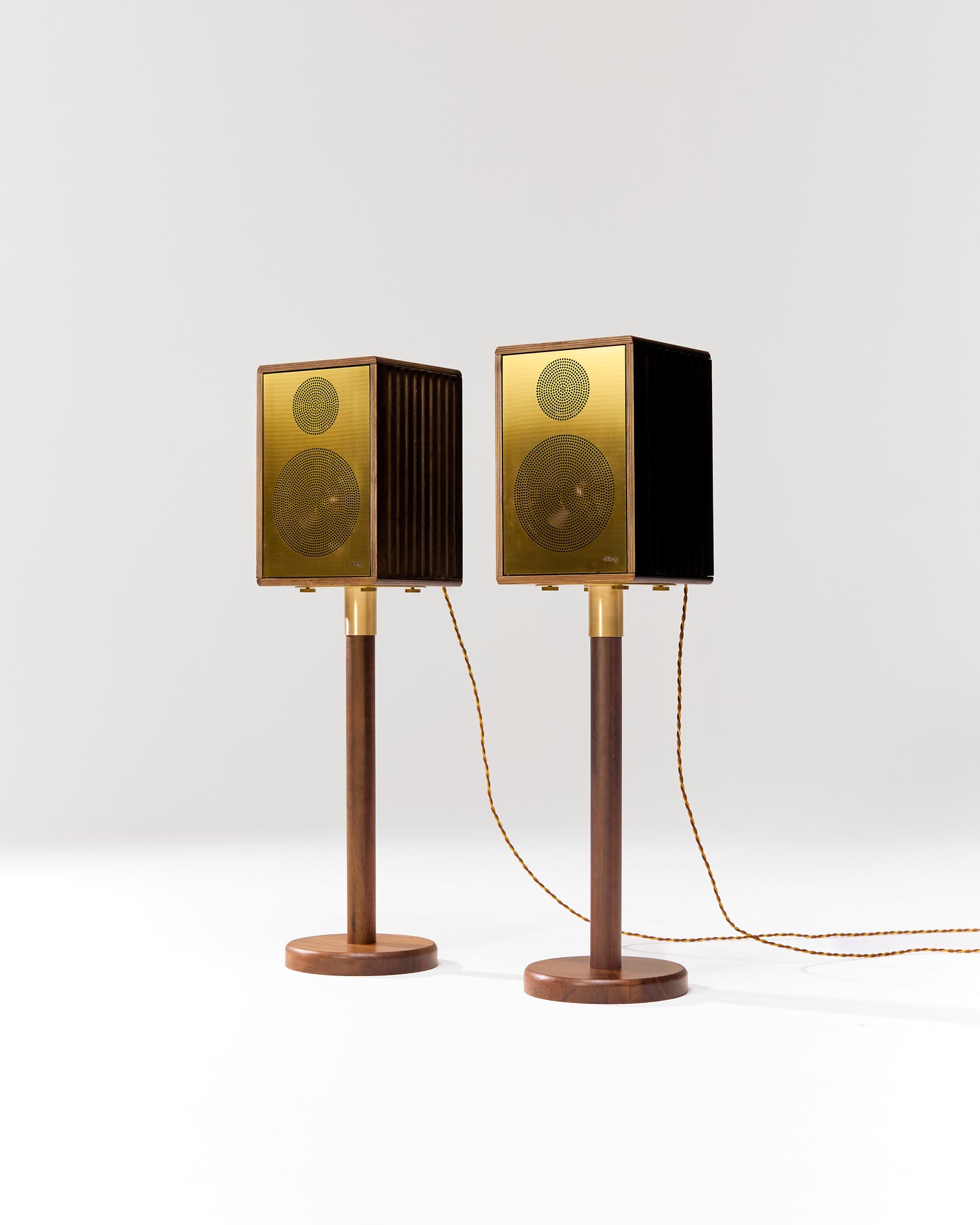 Pair of gold speakers on stands against a white background